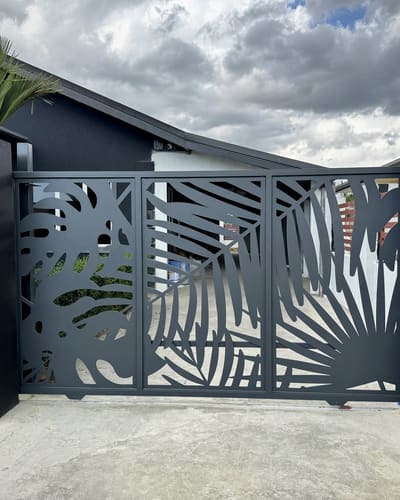 Charcoal driveway gate with palm and monstera leaves cut through the panels