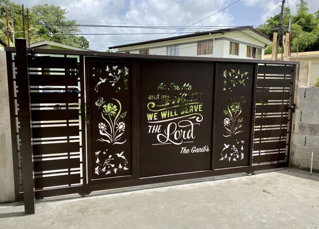 A driveway gate with a scripture verse and the family name cut through the steel