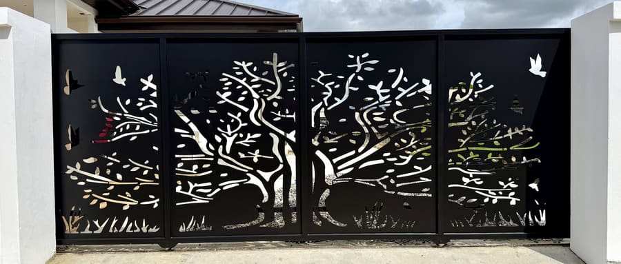 A four-panel driveway gate with a tree and birds cut through solid steel