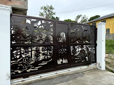 A driveway gate with a forest, a wolf and a moon cut across three panels