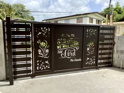 A driveway gate with a scripture verse and a family name cut through the steel