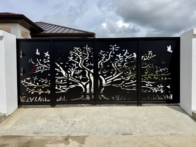 A four-panel driveway gate with a tree and birds cut through solid steel