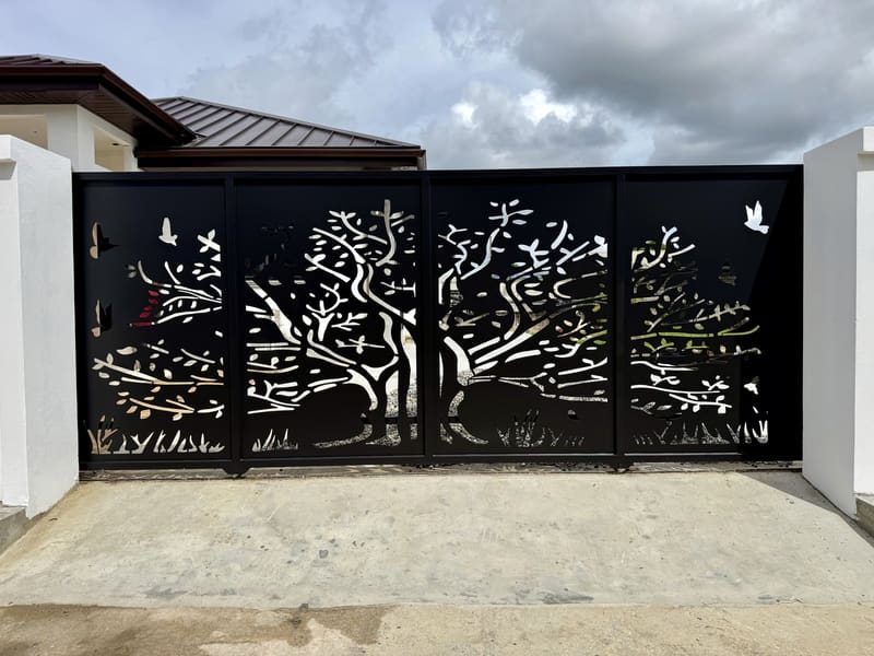 A four-panel driveway gate with a tree and birds cut through solid steel