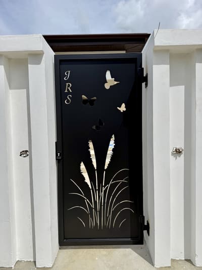 A pedestrian gate with a monogram, butterflies and reeds cut through the steel